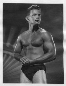 A classic black-and-white studio portrait of a muscular man posing in dark briefs.