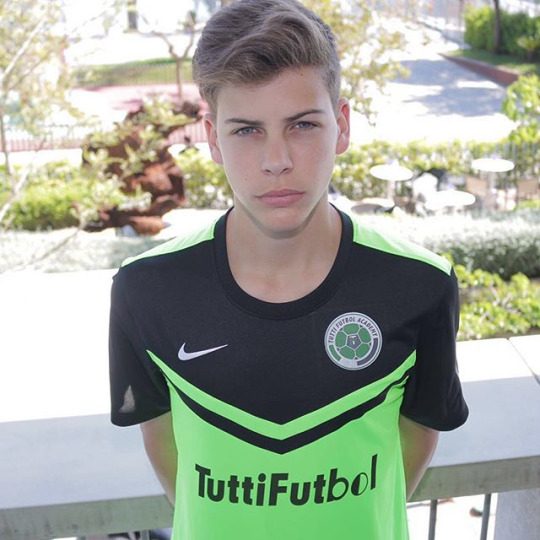 A smooth-faced young man wears a neon green and black football jersey while posing outdoors.