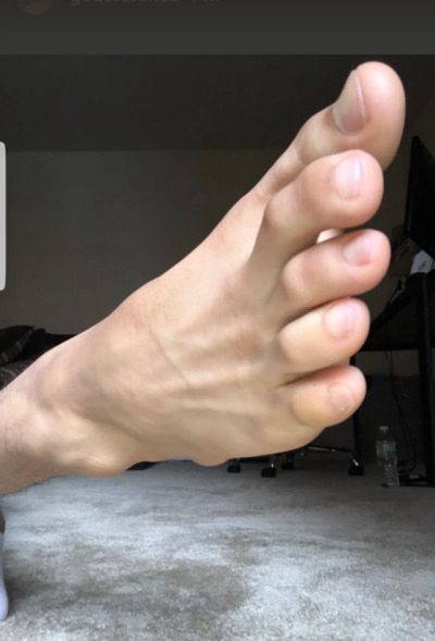 A close-up view of a bare male foot with toes spread, shown in an indoor residential setting.