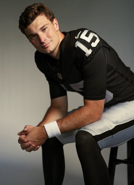 A young man in a full black and white football uniform sits on a stool against a plain background.