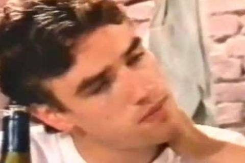 A close-up shot of a young, smooth dark-haired man wearing a white t-shirt indoors.