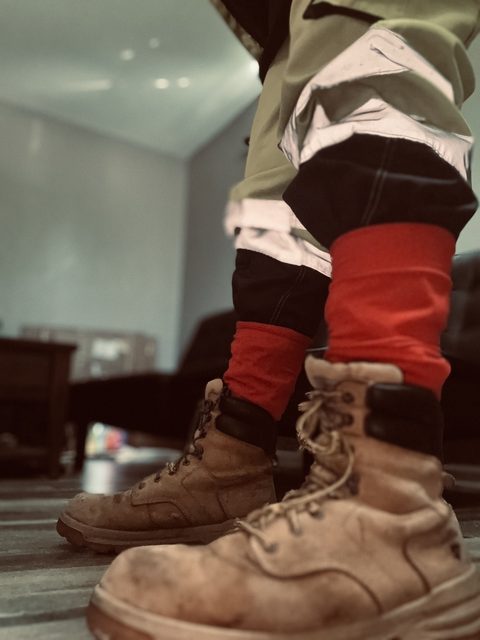 A person wearing tan work boots and red socks stands in high-visibility construction trousers with reflective strips.
