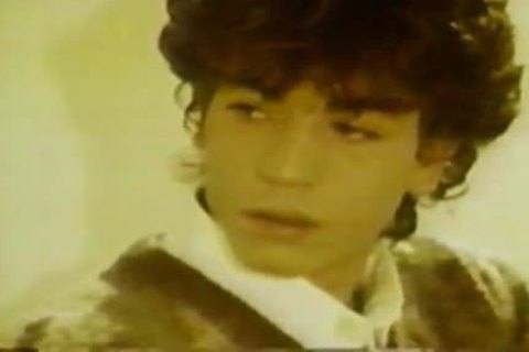 A close-up vintage portrait of a young man with dark curly hair looking off-camera.