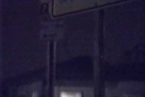 A grainy nighttime shot depicting street signage outdoors in a dark public setting.