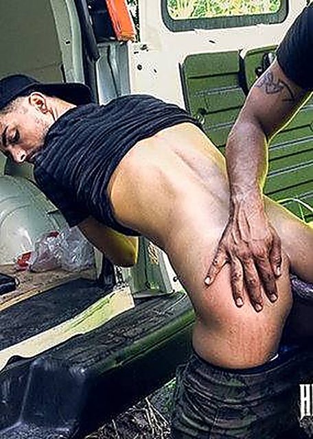 A man in camo pants bends over the open back of a van during an outdoor sexual encounter.