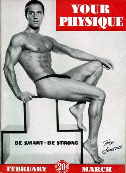 Vintage physique magazine cover featuring a muscular, smooth-skinned man in a posing strap seated on a geometric studio block.