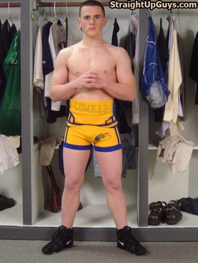 A muscular young man with a buzzcut poses in yellow and blue wrestling gear inside a locker room.