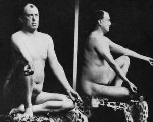 A historical black-and-white studio photograph depicting two views of a mature nude man seated on a patterned cloth.