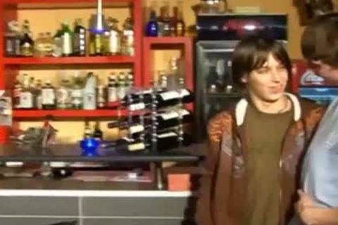 A young man wearing a brown jacket stands near a bar counter while interacting with another man.