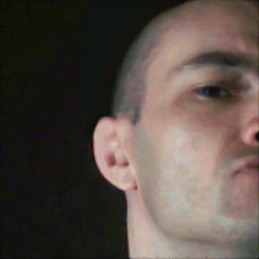 A close-up portrait of a man with a buzzcut looking into the camera against a dark background.