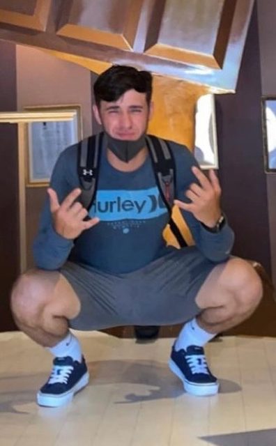 A muscular man in a long-sleeved shirt and gym shorts squats down, highlighting his legs and white tube socks.
