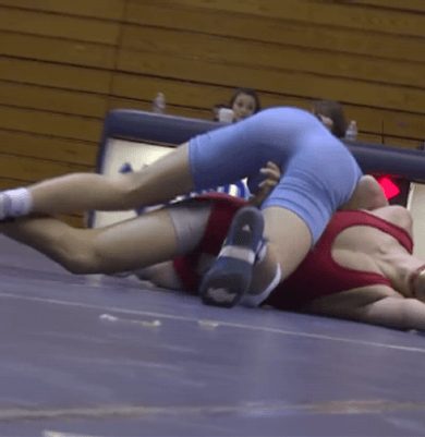Two men in form-fitting blue and red wrestling singlets grapple on a mat.