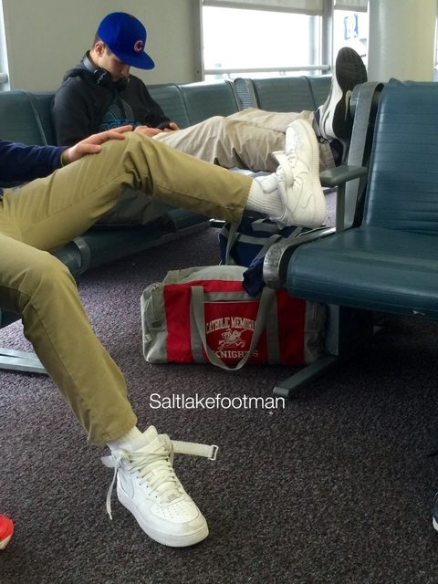 A man in khaki pants and white high-top sneakers relaxes in a public terminal, prominently displaying his white tube socks and footwear.