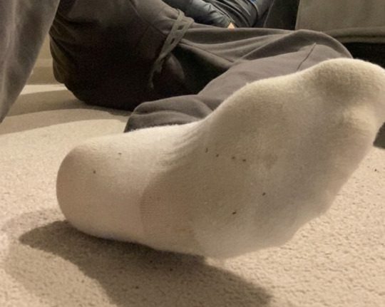 A foot wearing a white sock rests on a carpeted floor.