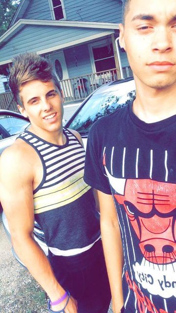 Two young men pose together outdoors in casual attire.