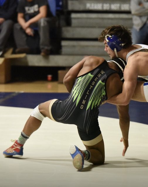 Two athletic wrestlers in singlets engage in a grappling match on a gymnasium mat.