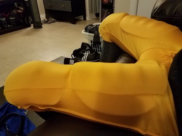 A point-of-view shot of a person wearing bright yellow padded football compression pants indoors.