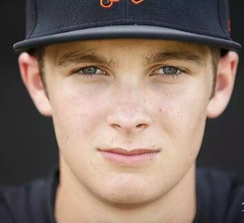 A young man with light eyes and a baseball cap looks directly at the camera.
