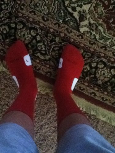 A POV shot shows a person's legs in light blue shorts and red athletic socks while standing on a patterned rug.