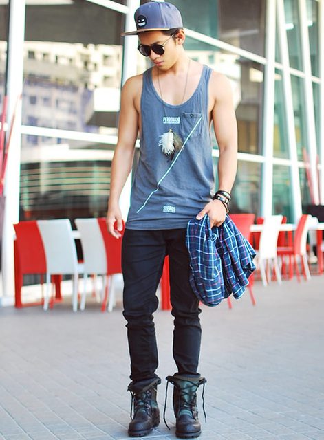 A smooth, lean twunk poses outdoors wearing a gray tank top, black jeans, and prominent combat boots.