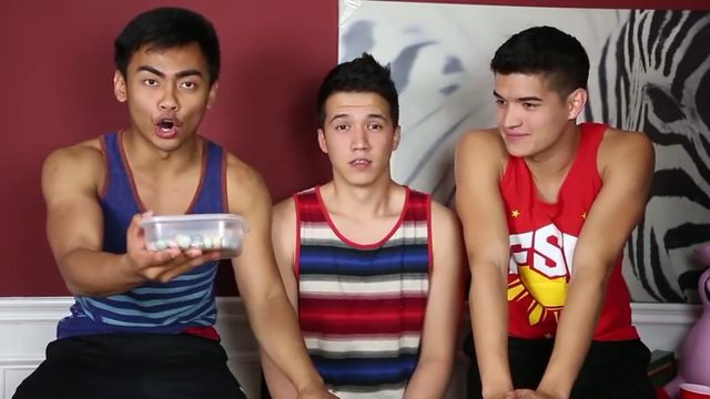 Three young men in tank tops are engaged in a casual indoor activity.