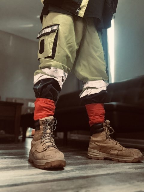 A man wears high-visibility construction pants tucked into red socks and tan work boots in an indoor setting.