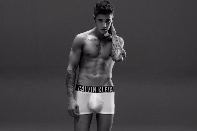 A young man poses shirtless in white boxer briefs with a prominent waistband.