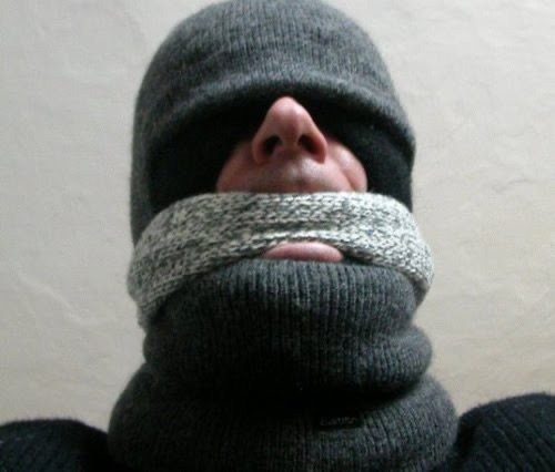 A man's head is heavily wrapped in thick grey knitted wool, acting as a functional blindfold and mouth gag.