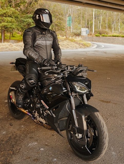 A man wearing a full Alpinestars leather motorcycle suit and an AGV helmet sits on a black BMW motorcycle.