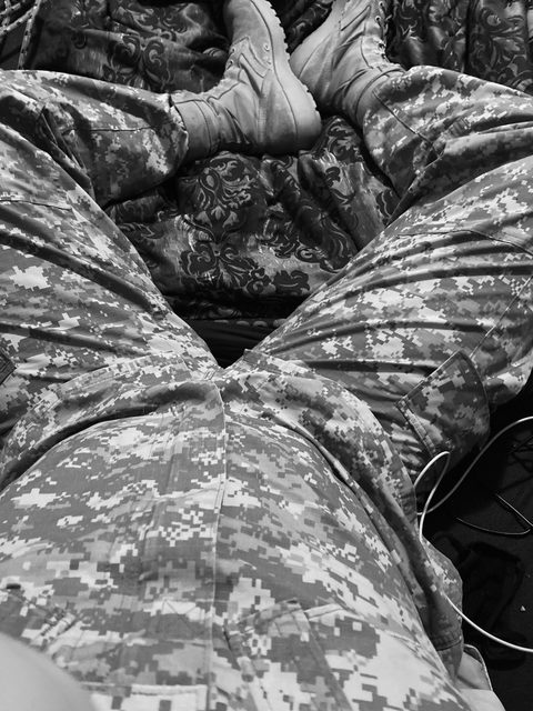 A POV view looking down at a person lying back in a digital camouflage military uniform and combat boots.