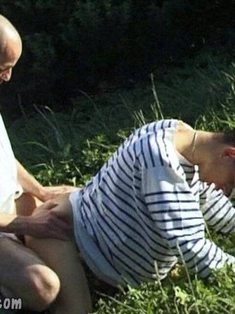Two men engage in an intimate outdoor encounter while surrounded by grass and foliage.