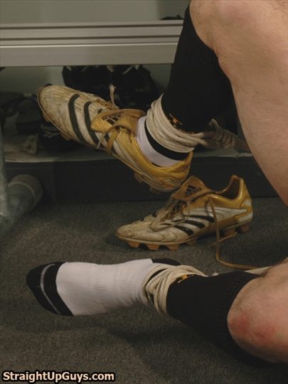 A view of a man's legs and feet bound at the ankles with rope while wearing socks and gold football boots in a locker room.