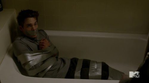 A young man lies bound with heavy silver duct tape around his arms and legs while gagged inside a bathtub.