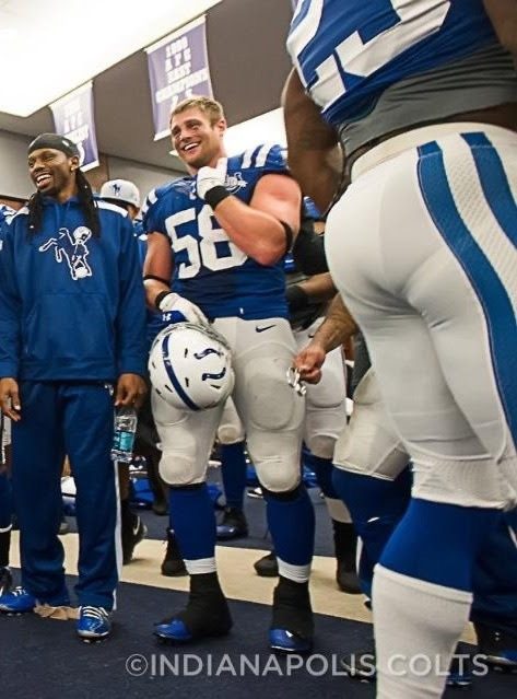 American football players wearing tight uniforms and gear inside a locker room.