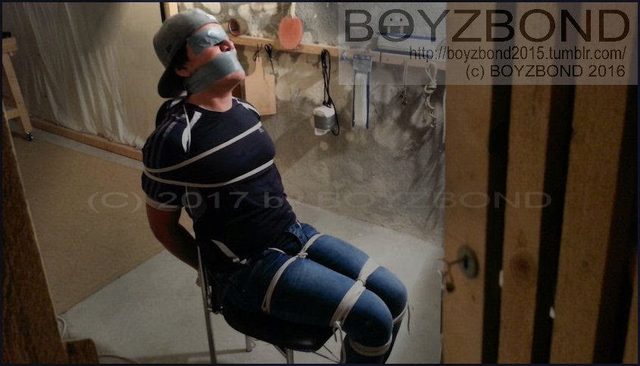 A young man is bound to a chair with rope and gagged with duct tape in a basement dungeon setting.