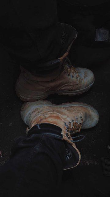 A POV shot looks down at a pair of worn, dirty tan leather work boots resting on a dark vehicle floor.