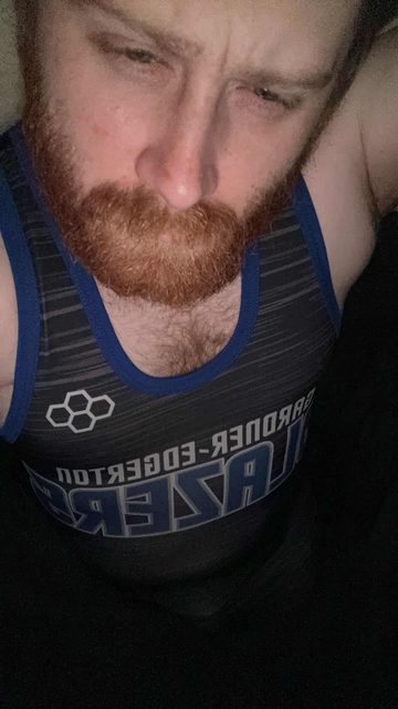 A man with a red beard and hairy chest is wearing a black and blue sportswear tank top.