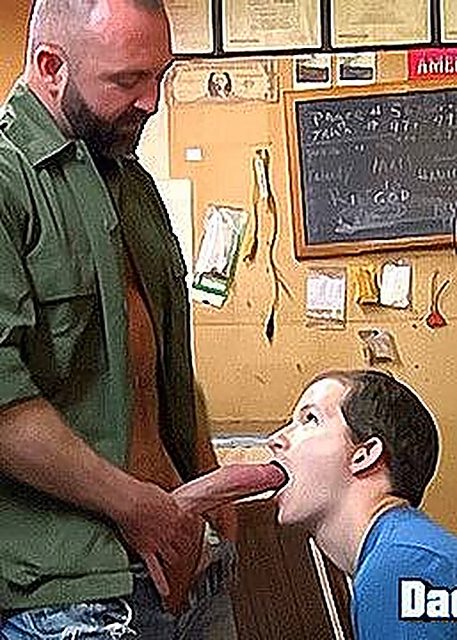 A bearded older man in an unbuttoned green shirt guides his exposed penis into the open mouth of a kneeling younger man.