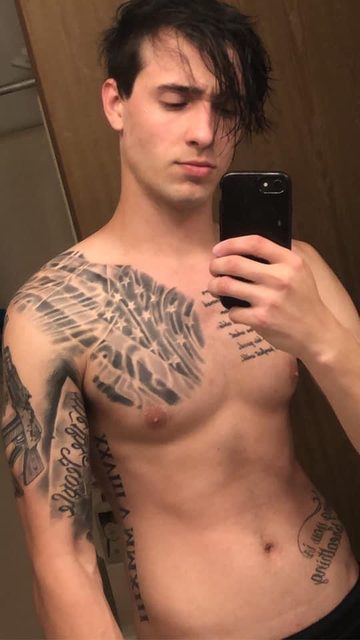 A shirtless young man with extensive chest and arm tattoos takes a mirror selfie.