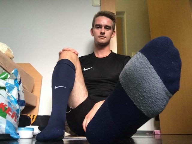 A young man wearing a black Nike football kit and tall socks sits on the floor with one foot extended toward the camera.