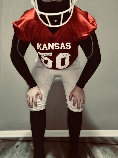 A man wearing a full red and white American football uniform, including a helmet and black compression gear, poses indoors.
