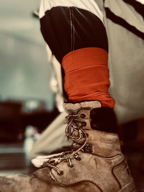 A close-up view focuses on a worn brown leather work boot worn with bright red socks.