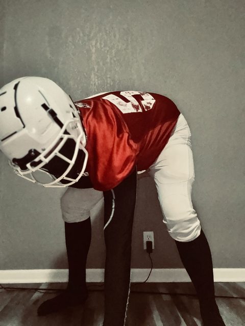A person in a full American football kit, including a helmet, jersey, and padded pants over compression tights, leans forward in a presenting stance.