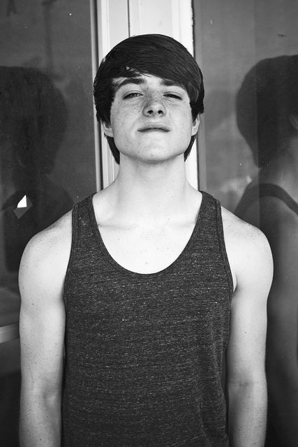 A young man with freckles poses in a tank top.