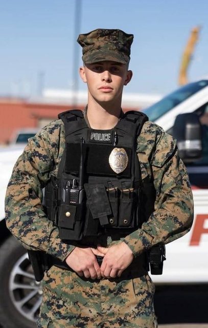 A young man in a camouflage military police uniform wears a tactical vest with a badge and radio while standing outdoors.
