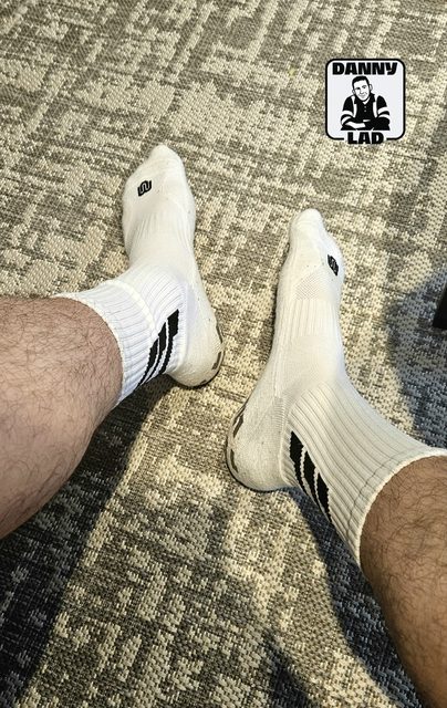 A pair of hairy legs are shown wearing white athletic crew socks with black stripes on a patterned carpet.
