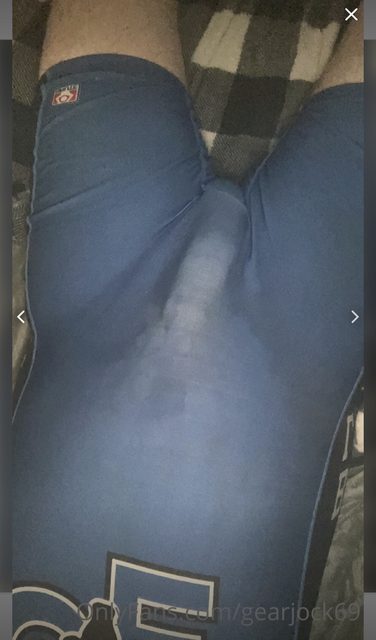 A man lies on a bed wearing blue compression shorts with a visible bulge.