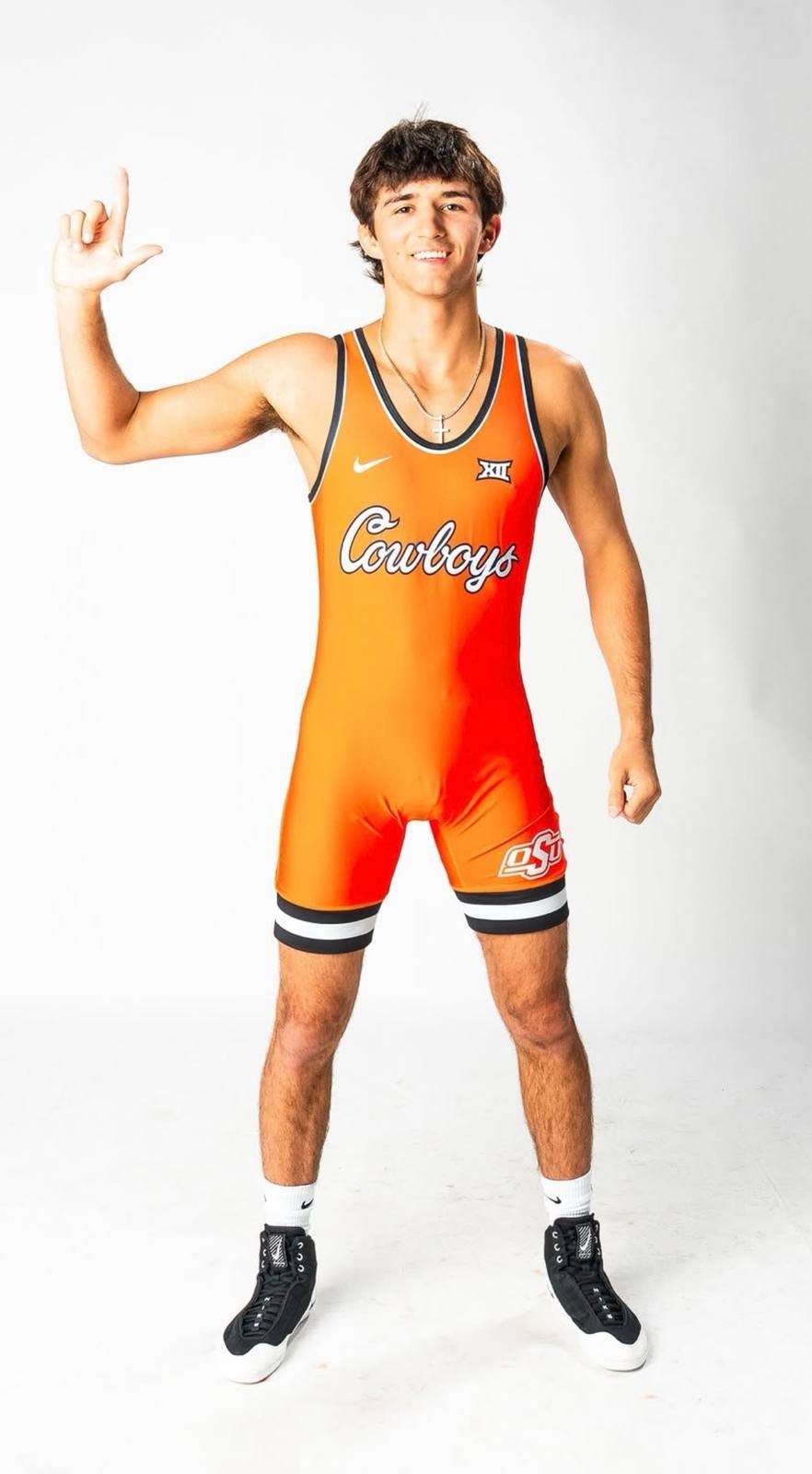 A fit young man poses in a bright orange wrestling singlet and black wrestling shoes against a white background.