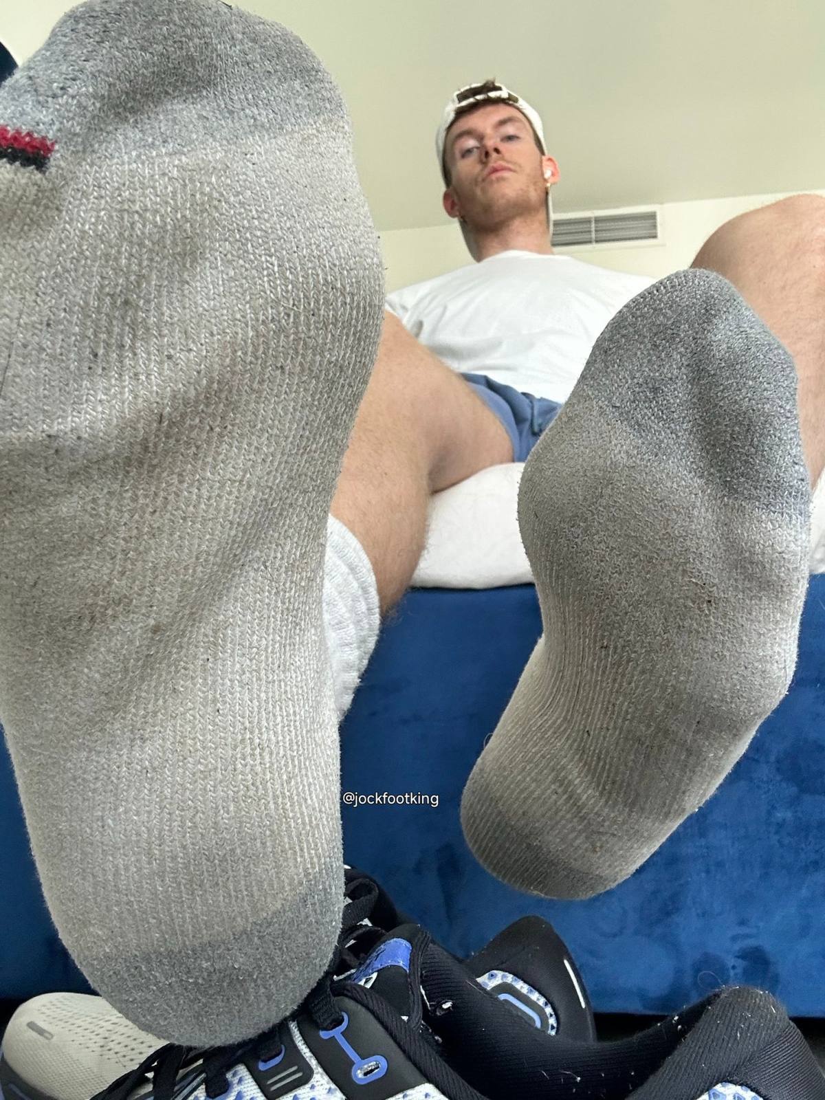 A man in athletic gear sits back, displaying his dirty white and grey socks close to the camera.