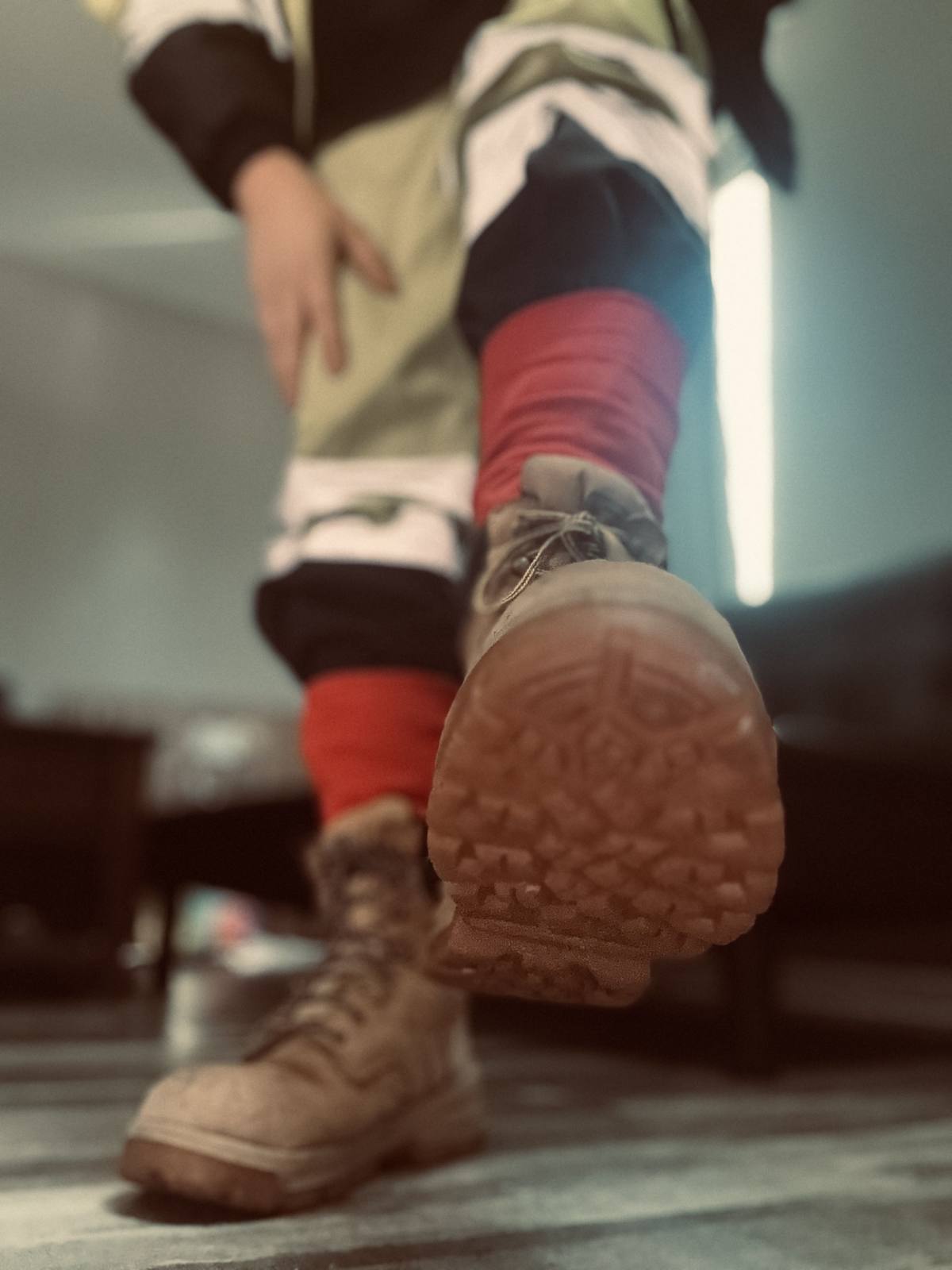 A low-angle POV shot captures a person wearing tan work boots and red socks, with one boot lifted towards the viewer.